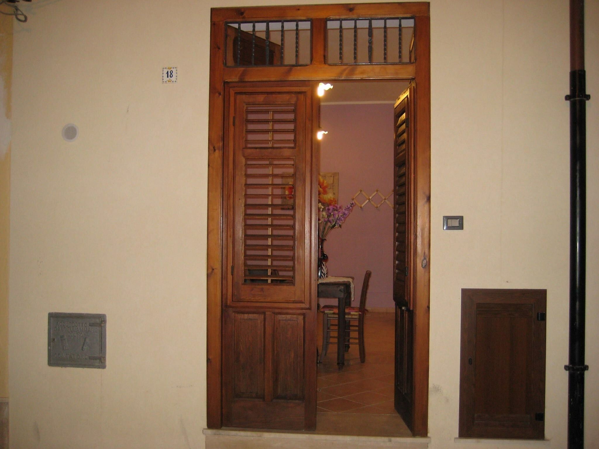 Una puerta doble de madera con un ventanal pequeño, suelo de baldosas y una silla al fondo.