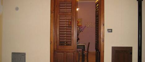 Una puerta doble de madera con un ventanal pequeño, suelo de baldosas y una silla al fondo.