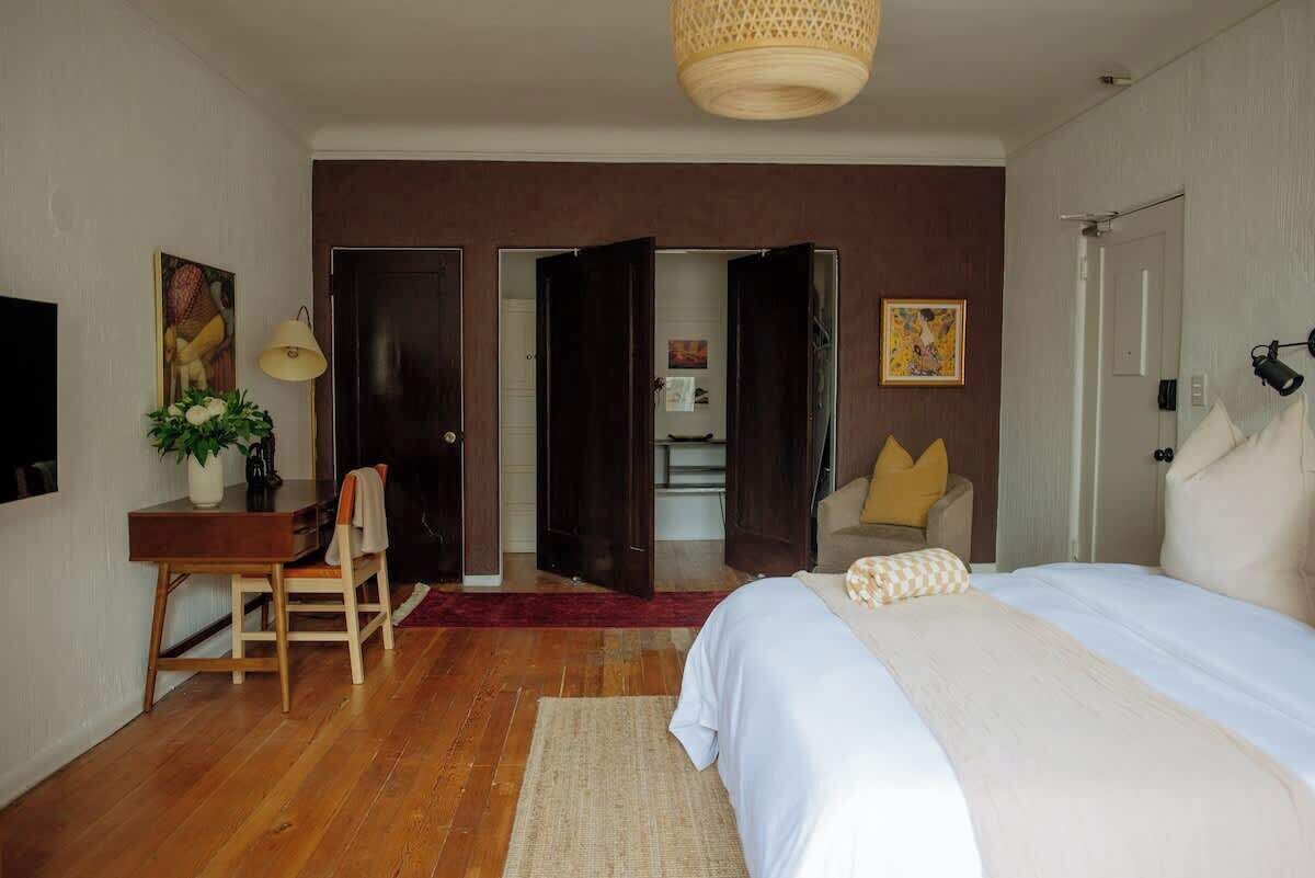 Un dormitorio con cama, escritorio, silla y puerta abierta que da a un baño.