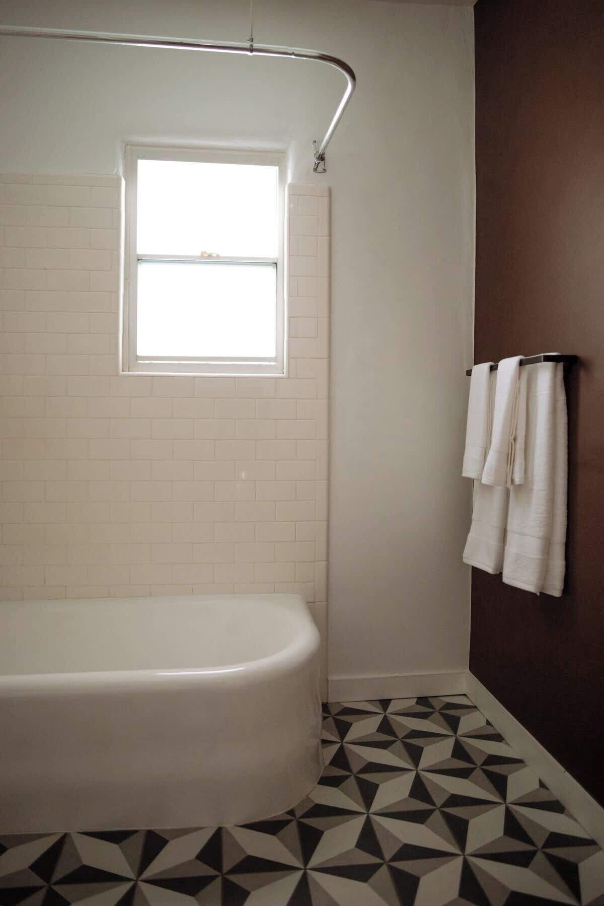 A bathroom with a white bathtub, a window, and a geometric patterned floor.