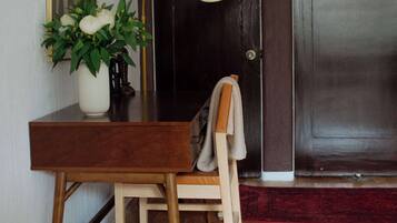 A wooden desk with a vase of flowers, a lamp, and a chair in a room with wooden flooring and dark doors.
