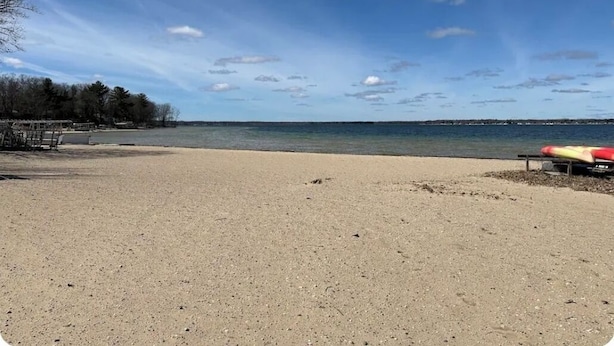 Una playa arenosa con un banco y un kayak rojo y amarillo.