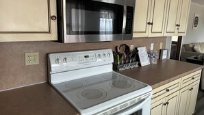 Una cocina con microondas de acero inoxidable, estufa blanca y armarios color beige. Hay una encimera con una botella de agua y un cartel que dice "eat & drink".