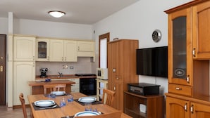 A compact kitchen with wooden cabinets, a dining table set for two, and a television mounted on the wall. - Casa delle Vigne by Wonderful Italy (Olbia)