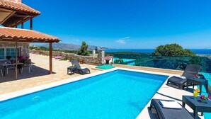 Zona de piscina con sillones de descanso y vista al mar.
