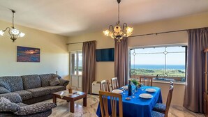 Una sala de estar con sofá, mesa de comedor y sillas, una araña y un ventanal con vistas.