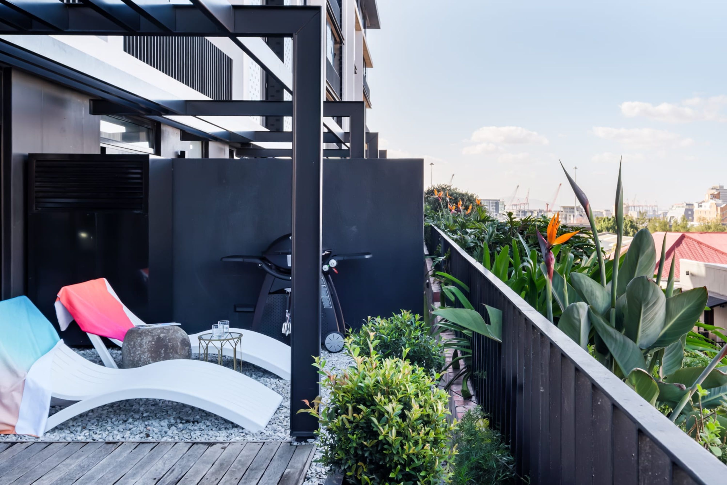Eine Dachterrasse mit Liegestühlen, einem kleinen Tisch und einem Grillbereich.
