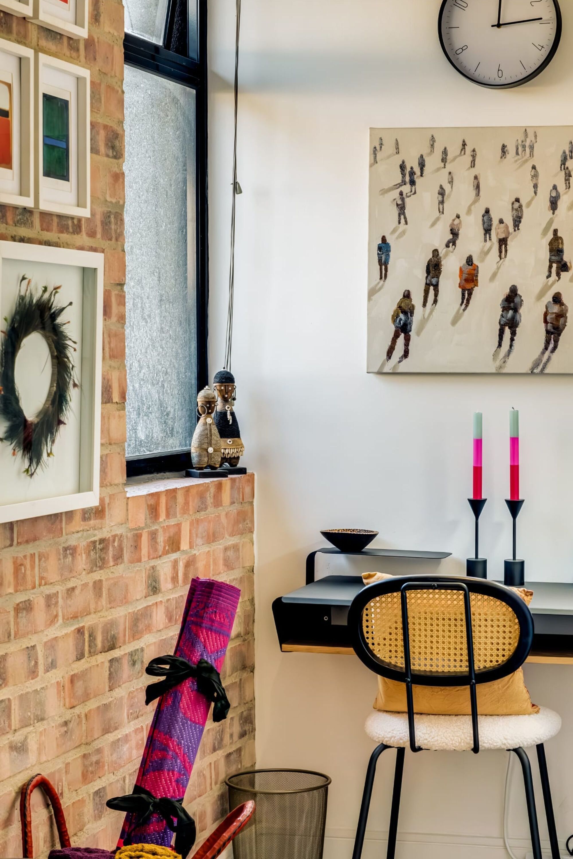 Una habitación con pared de ladrillo, ventana, reloj, pintura, silla y mesa con velas.