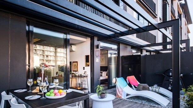 An outdoor patio with a dining table set for two, surrounded by white chairs. A white round table with a potted plant is also visible. - Contemporary Charming Apartment The Urban Edge (Cape Town)