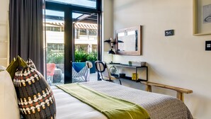 A hotel room with a bed, a desk, a chair, a window with curtains, a view of the outside, and a framed picture on the wall. - Contemporary Charming Apartment The Urban Edge (Cape Town)