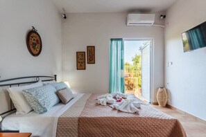 A bedroom with a bed, pillows, a quilted bedspread, a wall-mounted air conditioner, a television, and a sliding glass door leading to an outdoor area.