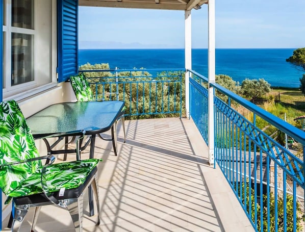 Een balkon met een glazen tafel en stoelen, met uitzicht op de kust.