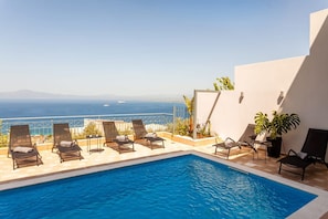 Zona de piscina con sillones de descanso y vista al mar.