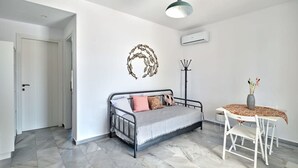 A modern bedroom with a bed, a coat rack, a table with a vase, and a decorative wall piece. - Villa Maria - Naoussa Fishes Blue Grey Suite (Paros)