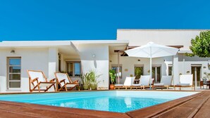 A pool area with lounge chairs and umbrellas, surrounded by a white building with large windows. - Chania Paradise Retreat-falasarna Villa Nostalgia (Kissamos)