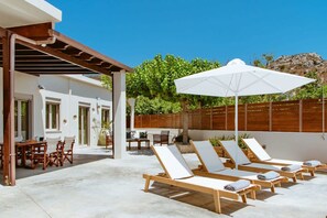An outdoor patio with lounge chairs and a table, a pergola, and a wooden fence.