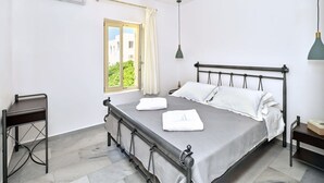 Un dormitorio con cama, ventilador de techo, aire acondicionado, ventana con cortinas, mesita de noche y velador.