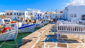 Un puerto con edificios blancos, barcos amarrados y un paseo pavimentado con piedra.