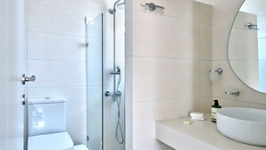 Un baño moderno con inodoro, ducha con cerramiento de vidrio y lavamanos con espejo.