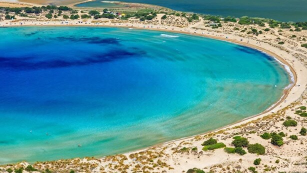 Vista aérea de una zona costera con una playa extensa, aguas azul turquesa y vegetación escasa.