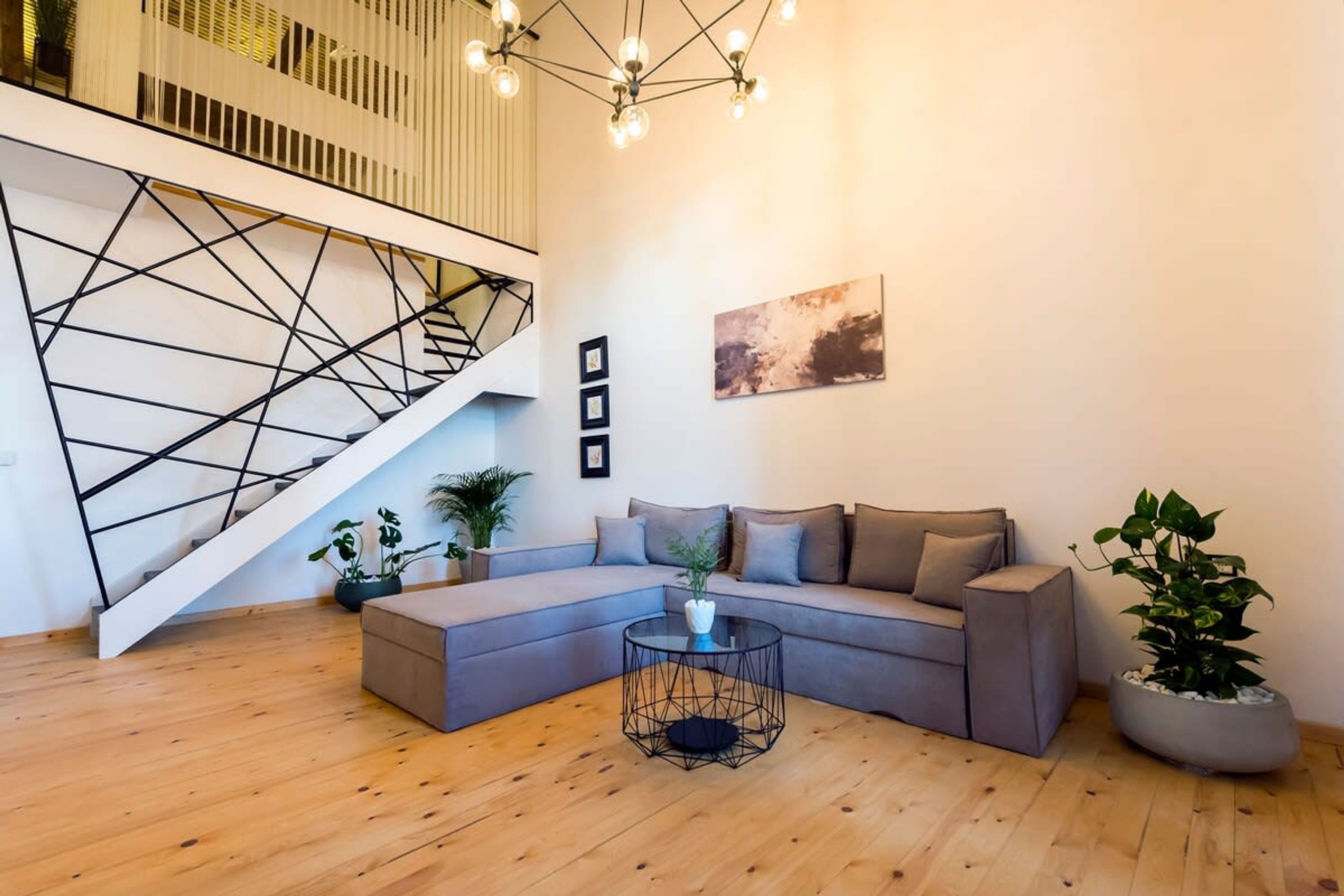 A modern living room with a grey sectional sofa, a round coffee table, and a staircase with a geometric railing.