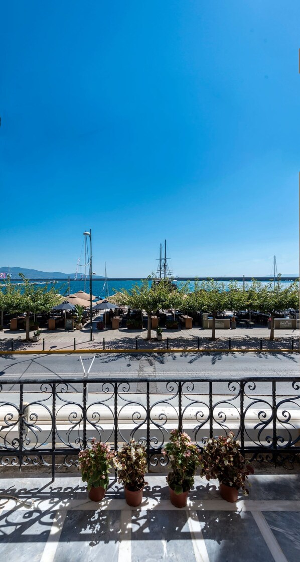 Un balcon agrémenté de plantes en pot, une vue dégagée sur la mer et, au loin, un port de plaisance avec des bateaux.
