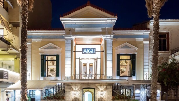 A building with a sign reading "AIGLI" at the entrance, featuring a stone facade, a tiled roof, and a central entrance with a staircase. - Aigli Seafront Loft-luxury Design Retreat (Kalamata)