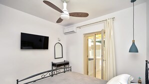 Une chambre à coucher comprenant un lit, un ventilateur de plafond, un appareil de climatisation, une télévision, un miroir et une porte donnant sur une autre pièce.