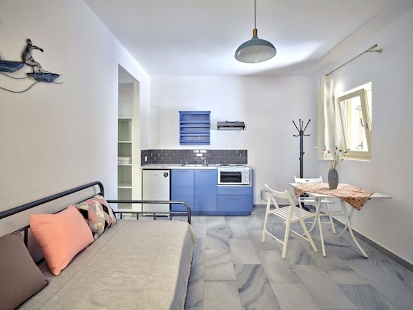 Une pièce de taille modeste comprenant un lit, une petite kitchenette, un coin repas et une fenêtre avec des rideaux.