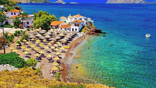 A coastal area with a beach, umbrellas, and buildings. - A Sea-licious Vacation - Chic Style in Hydra (Hydra)