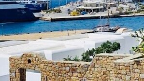 A coastal area with a large cruise ship docked at a pier, a stone wall, and a building with a flat roof. - Mykonos Violet Nest - Sea View Escape (Mykonos)