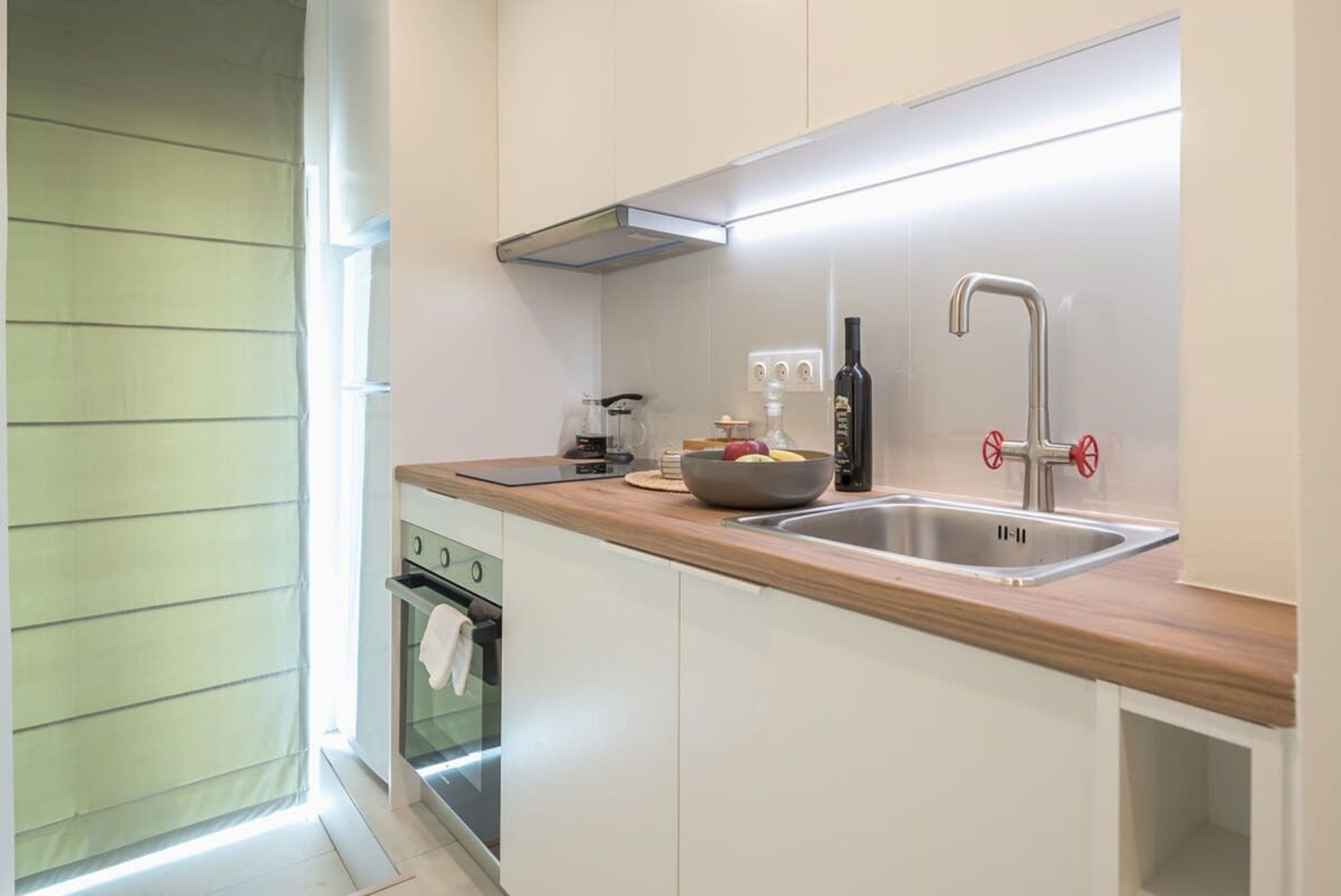 Una cucina moderna con mobili bianchi, un piano di lavoro in legno, un lavello in acciaio inossidabile e un forno integrato.
