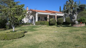 A house with a red-tiled roof, a covered porch, and a well-maintained garden with various shrubs and a palm tree.