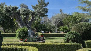 A landscaped garden with manicured hedges, a statue, and a view of a mountain.