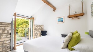 A bedroom with a large bed, a hanging swing, a stone wall, and a view of greenery outside. - Host Stay Sunnyside Barn (Bridlington)