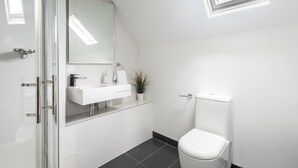A modern bathroom with a glass shower enclosure, a white sink with a mirror above it, and a toilet. - Host Stay Sunnyside Barn (Bridlington)