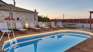 Une piscine extérieure entourée de murs en pierre et dotée d’une terrasse en bois, avec des chaises longues et des parasols.
