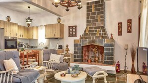Un vaste espace de vie agrémenté d’une cheminée en pierre, de meubles en bois et d’une cuisine située au fond de la pièce.