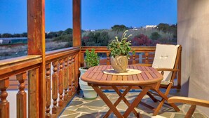 Une terrasse en bois avec une table ronde et deux chaises, un pot de fleurs et une vue sur un paysage naturel.