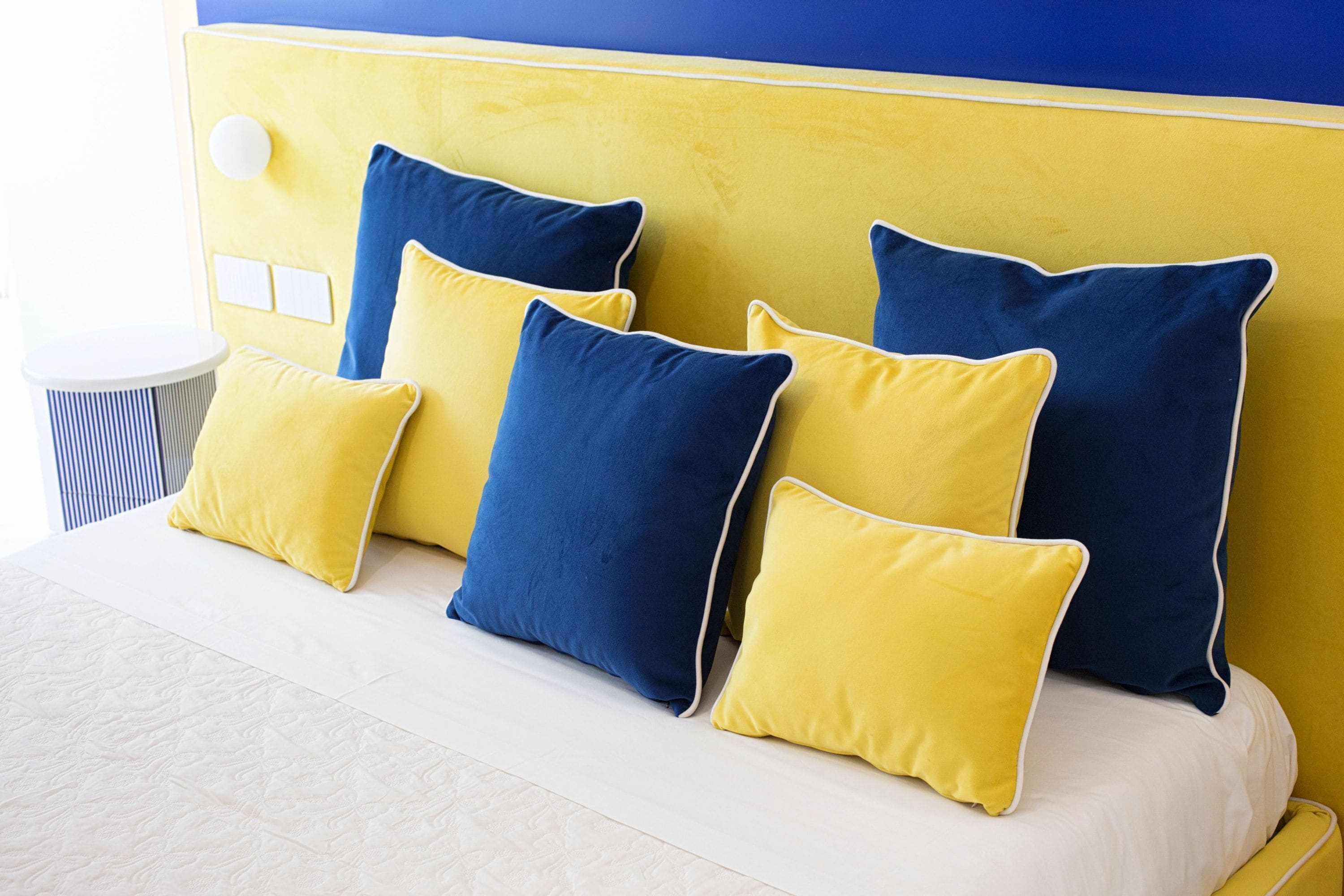 A bed with a yellow headboard and multiple pillows in yellow and blue.
