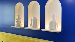 Três vasos brancos expostos em janelas em arco sobre um fundo azul.