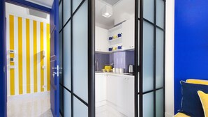 Una cocina moderna con armarios blancos, un electrodoméstico amarillo y una partición de vidrio con marco azul.