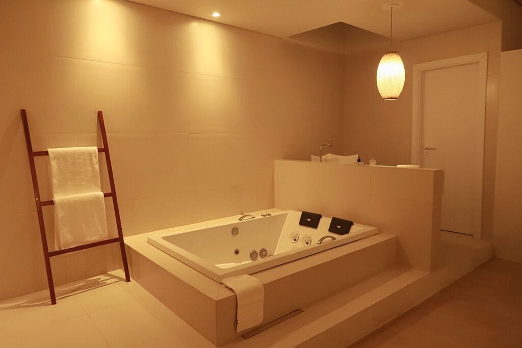 Ein modernes Badezimmer mit einer großen Badewanne, einem hölzernen Handtuchhalter, einem Waschbecken und einem Spiegel.