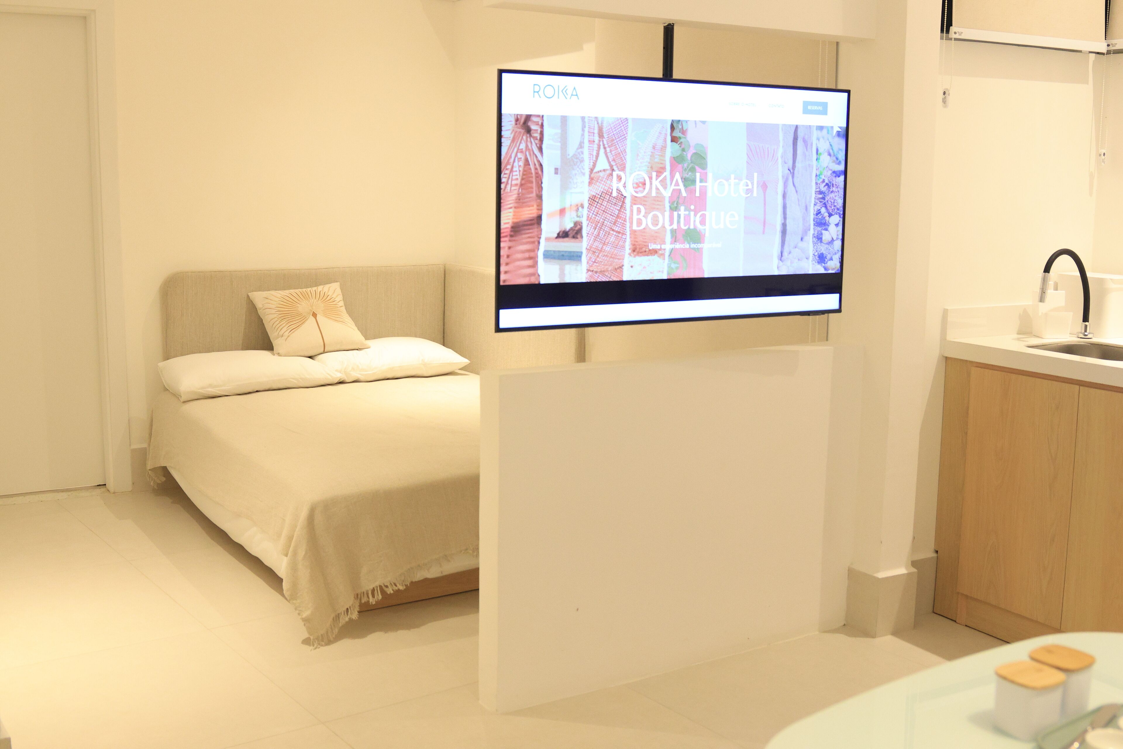 Une chambre d’hôtel comprenant un lit, un téléviseur fixé sur un support, une petite table avec un plateau en verre et une armoire en bois.