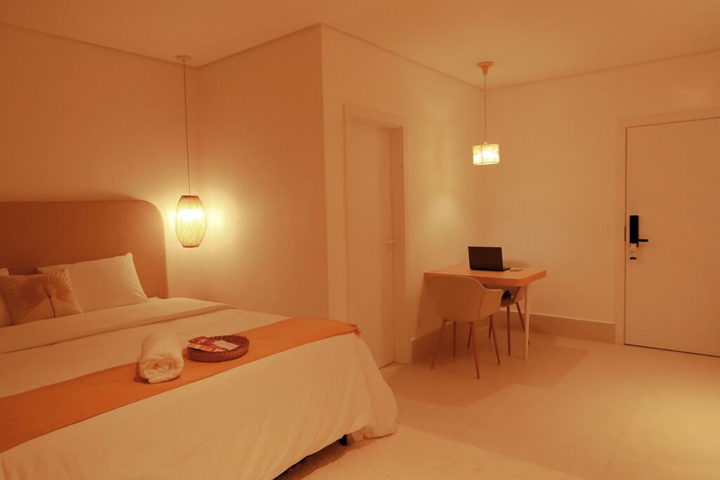 A hotel room with a bed, a desk with a laptop, and a door.