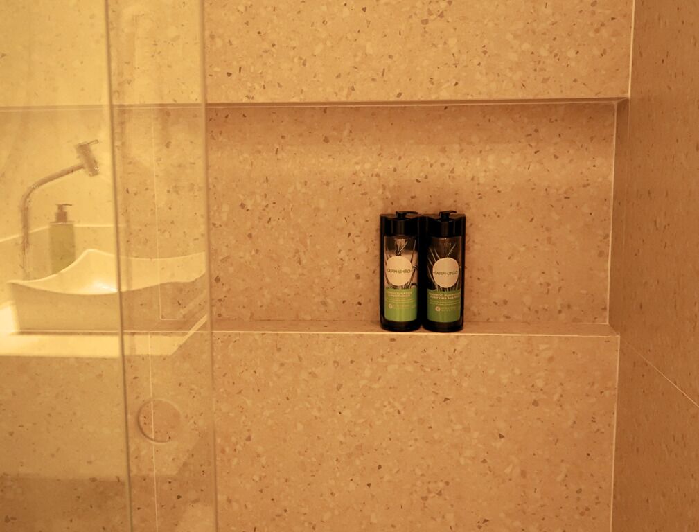 Een badkamer met een wastafel en twee flessen handzeep op een betegelde muur met spikkels.