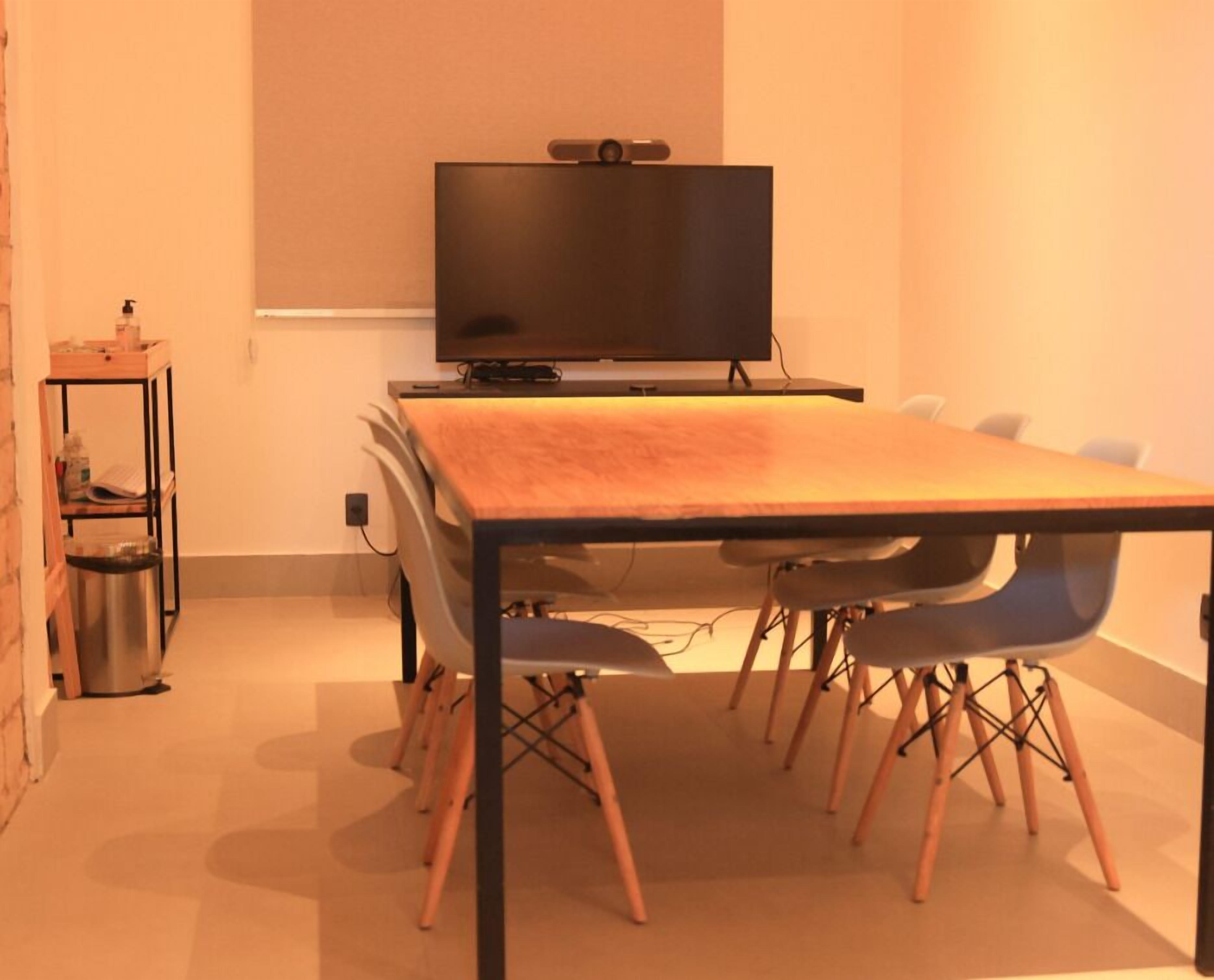 Un salón de conferencias con una mesa larga, sillas, un televisor y un estante con objetos.