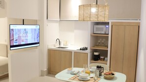 A modern kitchen with a dining area, featuring a flat-screen TV, a microwave, and a wicker hanging light fixture. - Roka Hotel Boutique (Boa Vista)
