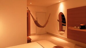 A room with a hammock, a bed, a mirror, and a shelf with toiletries. - Roka Hotel Boutique (Boa Vista)