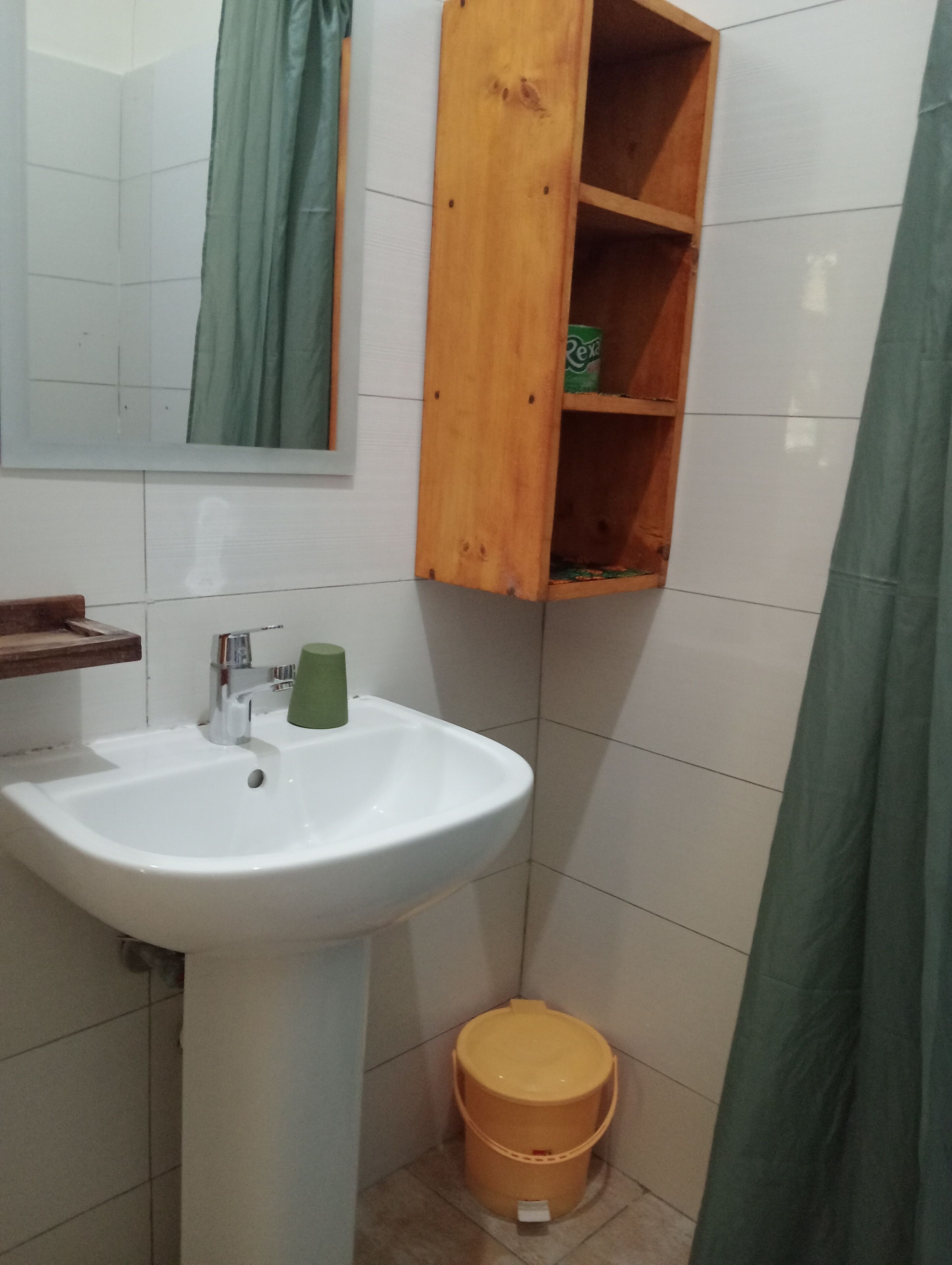 Un baño con un lavamanos blanco, un armario de medicinas de madera, una cortina de ducha verde y un cubo amarillo.